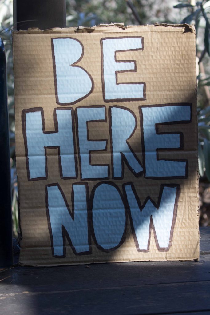 Sign with letters "Be here now"