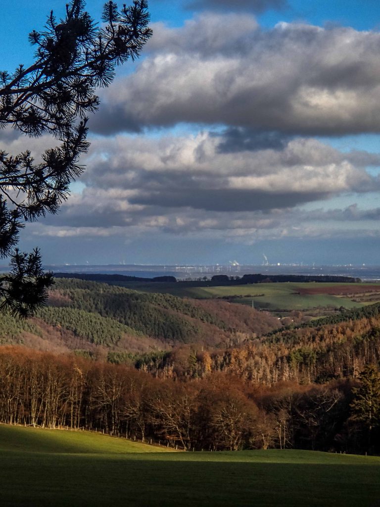 Clouds over hilly landscape, city and wind turbines in the distance